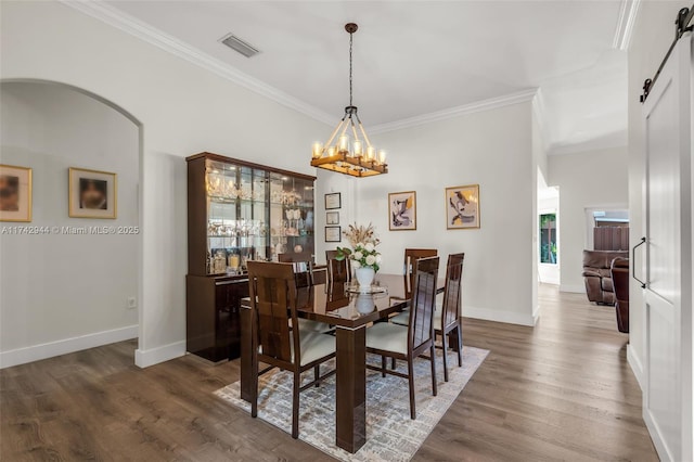 dining room featuring a barn door, ornamental molding, dark hardwood / wood-style flooring, and a chandelier