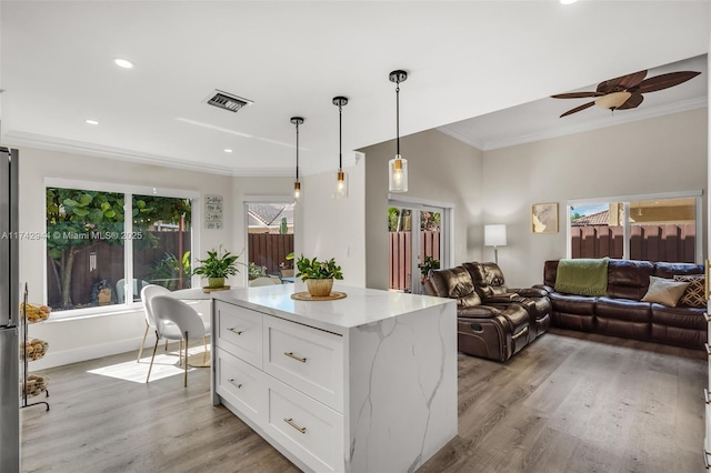 kitchen with pendant lighting, white cabinetry, ornamental molding, a center island, and light stone countertops