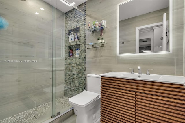 bathroom with tile walls, vanity, a shower with shower door, and toilet