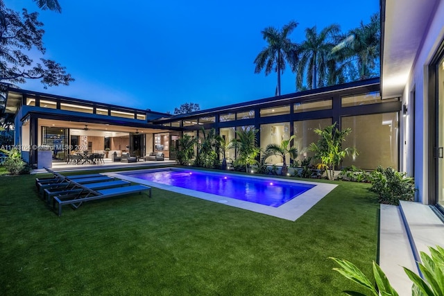 pool at dusk featuring a patio and a lawn