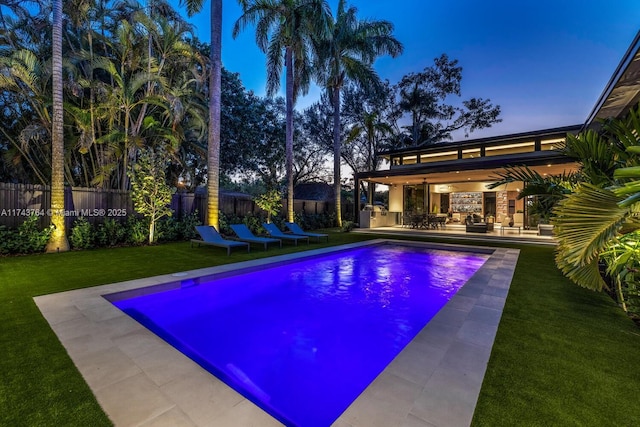 pool at dusk with a patio, area for grilling, and a yard