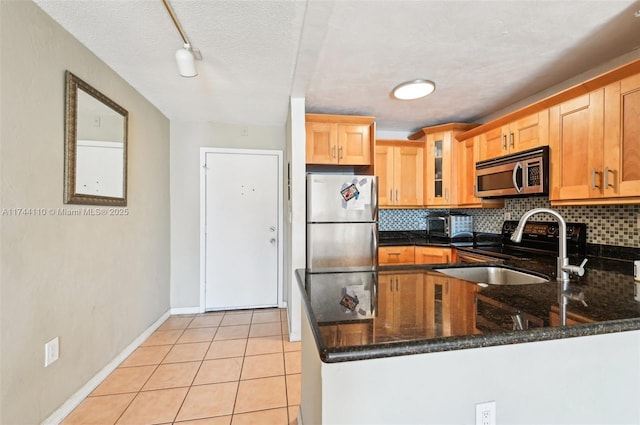 kitchen featuring light tile patterned floors, appliances with stainless steel finishes, kitchen peninsula, dark stone counters, and backsplash