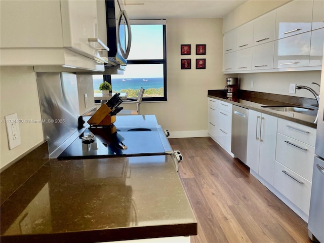 kitchen with sink, light hardwood / wood-style flooring, dishwasher, white cabinetry, and a water view