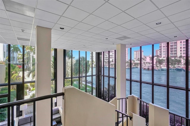 hall with a paneled ceiling, a healthy amount of sunlight, and a water view