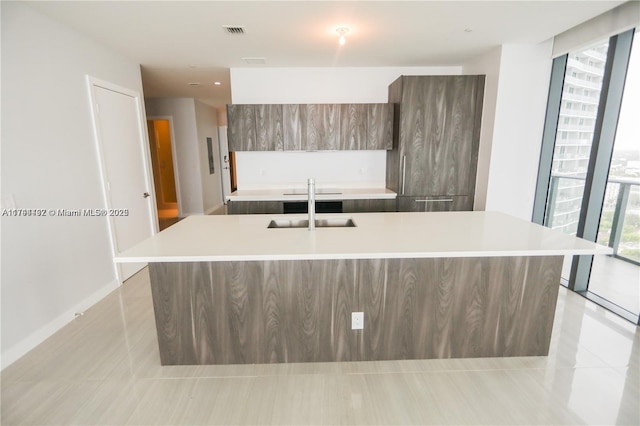 kitchen featuring sink, light tile patterned floors, floor to ceiling windows, and a center island with sink