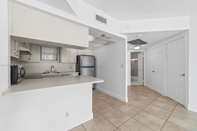 kitchen featuring sink, light tile patterned floors, stainless steel refrigerator, and kitchen peninsula