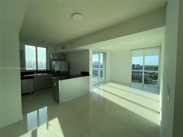 kitchen featuring dark countertops, light tile patterned floors, fridge with ice dispenser, and plenty of natural light