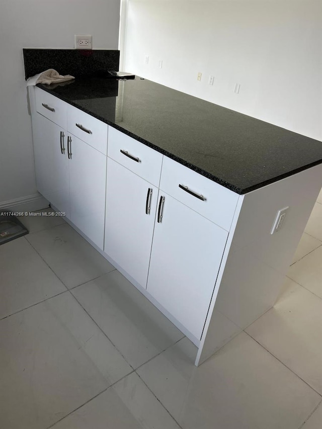 kitchen with light tile patterned floors, dark stone countertops, and white cabinets