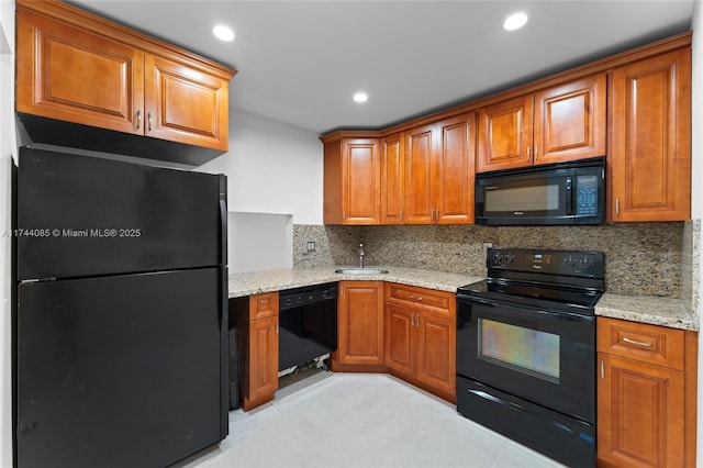 kitchen with light stone countertops, backsplash, black appliances, and sink