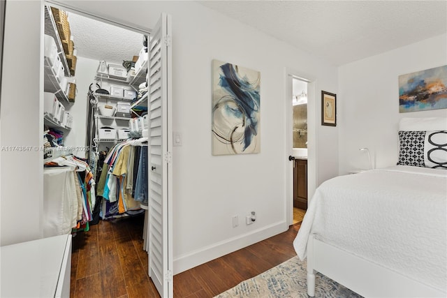 bedroom with a textured ceiling, a spacious closet, connected bathroom, and dark hardwood / wood-style floors