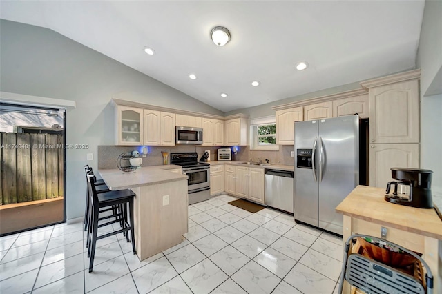 kitchen featuring lofted ceiling, a breakfast bar area, appliances with stainless steel finishes, kitchen peninsula, and backsplash