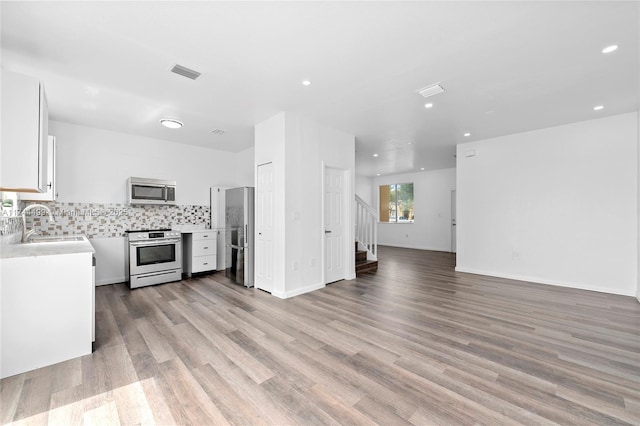 kitchen featuring sink, white cabinetry, light wood-type flooring, appliances with stainless steel finishes, and decorative backsplash