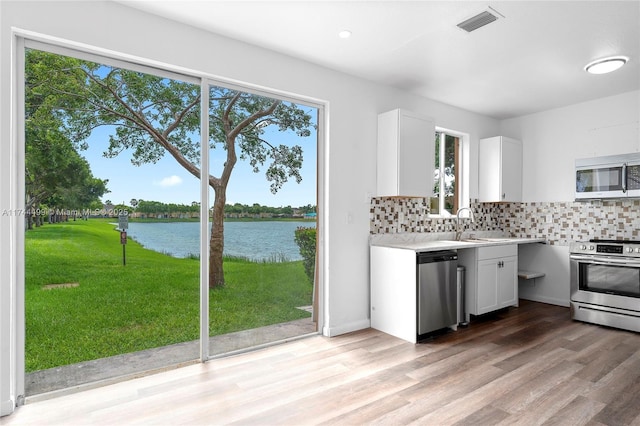 kitchen featuring stainless steel appliances, white cabinetry, a water view, and tasteful backsplash