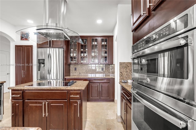 kitchen with tasteful backsplash, island exhaust hood, a center island, stainless steel appliances, and light stone countertops