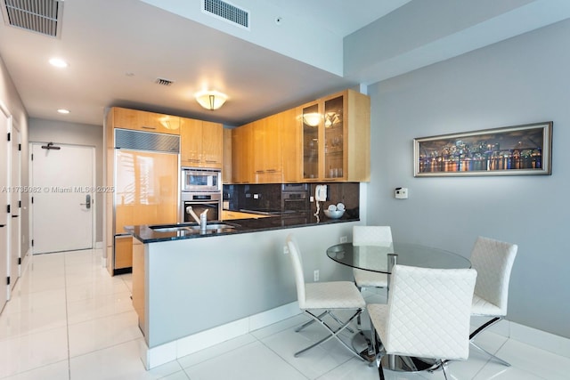 kitchen featuring sink, tasteful backsplash, built in appliances, light tile patterned floors, and kitchen peninsula