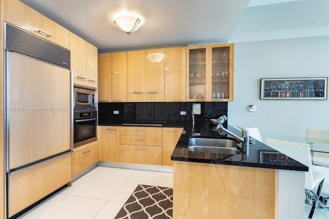 kitchen with sink, light tile patterned floors, built in appliances, light brown cabinetry, and kitchen peninsula