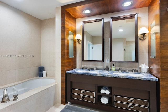 bathroom featuring tiled tub, vanity, and tile walls