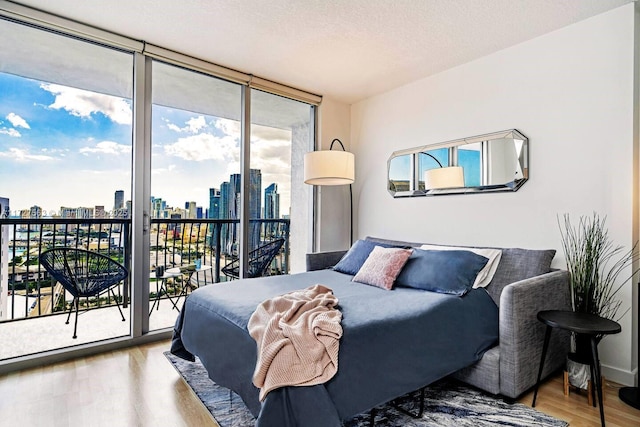 bedroom featuring expansive windows, access to exterior, light hardwood / wood-style flooring, and a textured ceiling