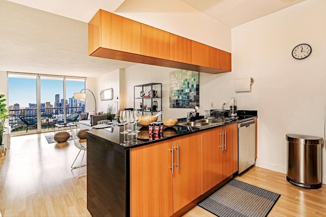 kitchen with sink, dishwasher, expansive windows, dark stone counters, and light hardwood / wood-style floors