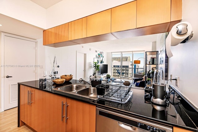 kitchen featuring sink, a wall of windows, dark stone countertops, stainless steel dishwasher, and light wood-type flooring