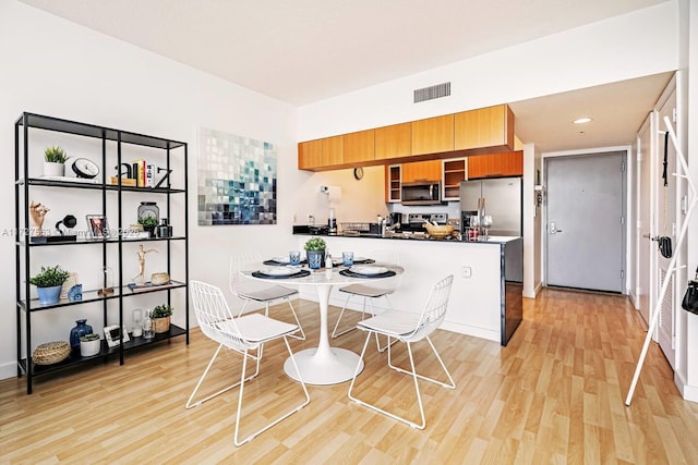 kitchen featuring light hardwood / wood-style floors, stainless steel appliances, kitchen peninsula, and a kitchen bar