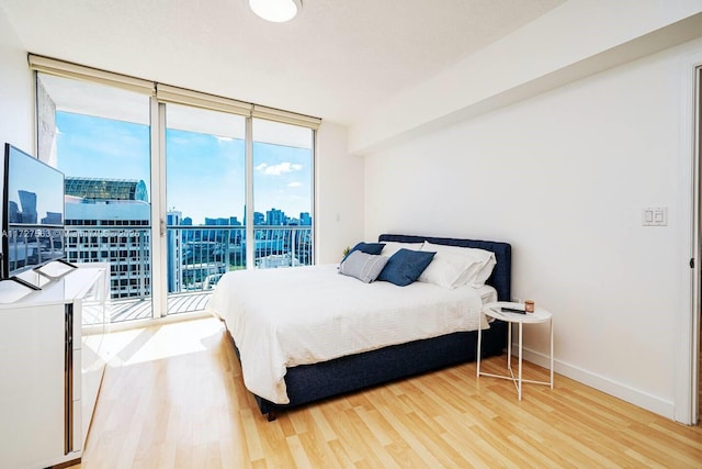 bedroom with expansive windows, wood-type flooring, and access to exterior