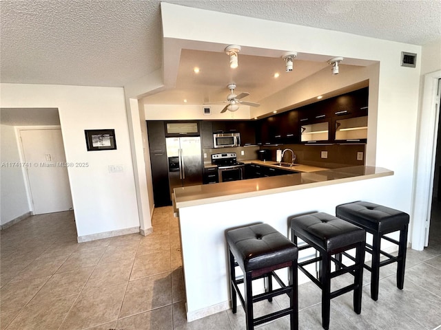 kitchen featuring sink, stainless steel appliances, a textured ceiling, light tile patterned flooring, and kitchen peninsula