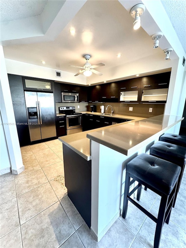 kitchen featuring a kitchen bar, light tile patterned floors, kitchen peninsula, ceiling fan, and stainless steel appliances