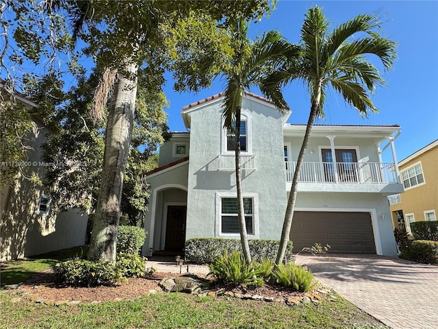 mediterranean / spanish home featuring decorative driveway, a balcony, an attached garage, and stucco siding