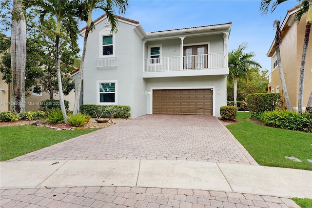 view of front of home featuring a front yard, decorative driveway, a balcony, and stucco siding