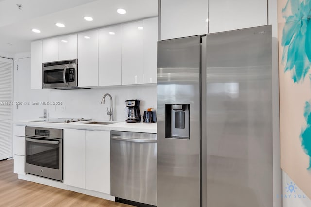 kitchen with stainless steel appliances, sink, light hardwood / wood-style flooring, and white cabinets