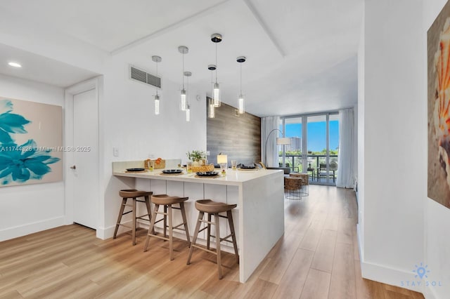 kitchen with pendant lighting, a kitchen bar, light hardwood / wood-style floors, kitchen peninsula, and floor to ceiling windows