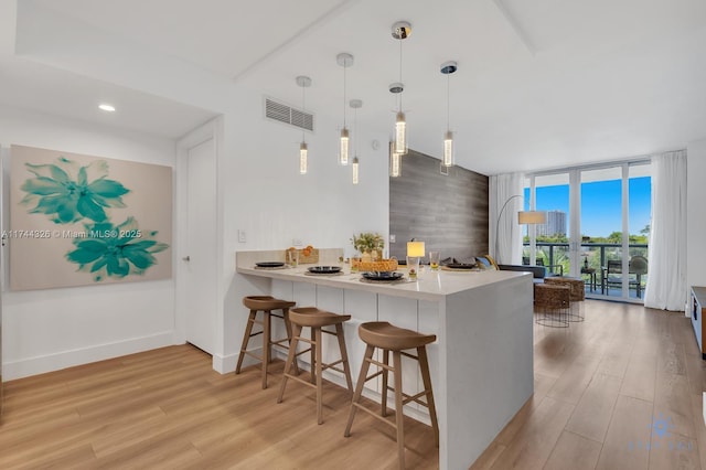 kitchen with hanging light fixtures, floor to ceiling windows, a kitchen bar, kitchen peninsula, and light wood-type flooring