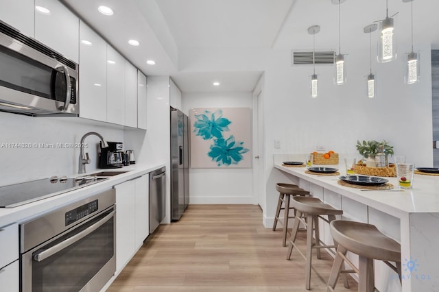 kitchen featuring appliances with stainless steel finishes, a breakfast bar, pendant lighting, and white cabinets