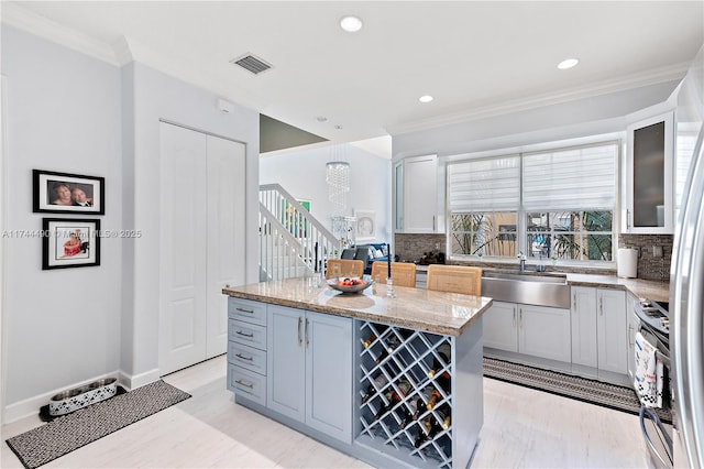 kitchen with sink, light stone counters, crown molding, a kitchen island, and decorative backsplash