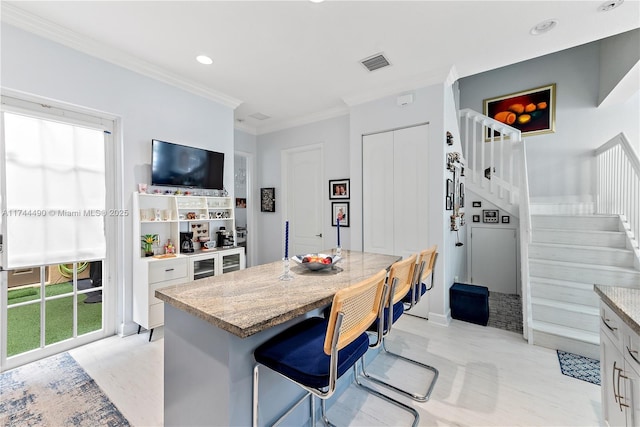 kitchen featuring a kitchen bar, crown molding, light stone counters, a center island, and white cabinets