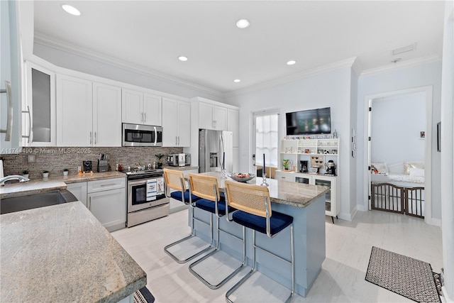 kitchen with white cabinetry, a kitchen breakfast bar, a kitchen island, stainless steel appliances, and light stone countertops