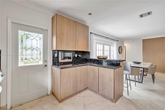 kitchen featuring light brown cabinetry, dark stone countertops, decorative backsplash, kitchen peninsula, and crown molding