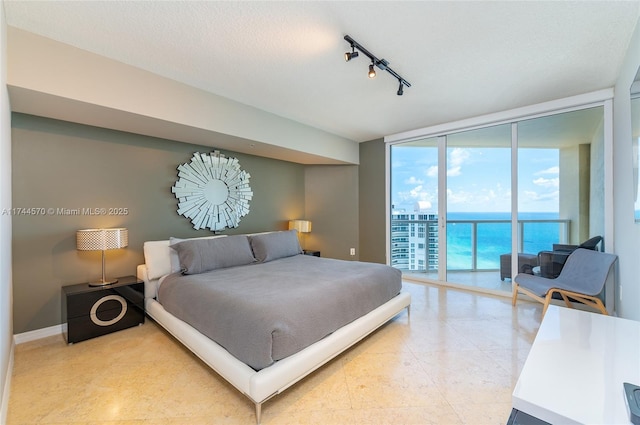 tiled bedroom featuring access to exterior, expansive windows, a textured ceiling, and a water view