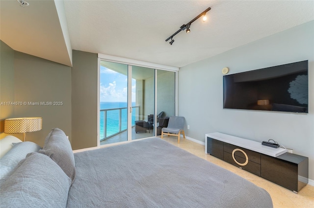 bedroom featuring floor to ceiling windows, rail lighting, a textured ceiling, light colored carpet, and access to exterior