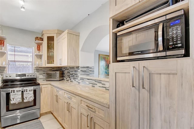 kitchen with light tile patterned floors, stainless steel appliances, light stone countertops, light brown cabinetry, and decorative backsplash