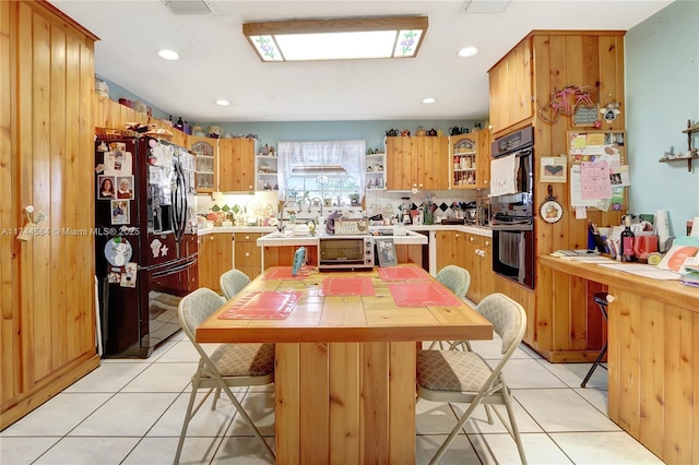 kitchen featuring light tile patterned floors, black appliances, a breakfast bar, and a kitchen island