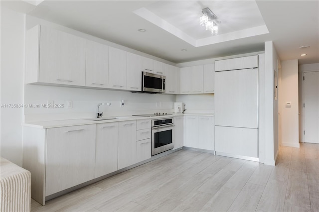 kitchen with appliances with stainless steel finishes, white cabinetry, sink, light hardwood / wood-style floors, and a tray ceiling