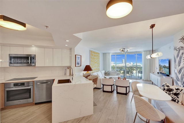 kitchen with sink, white cabinetry, hanging light fixtures, stainless steel appliances, and expansive windows