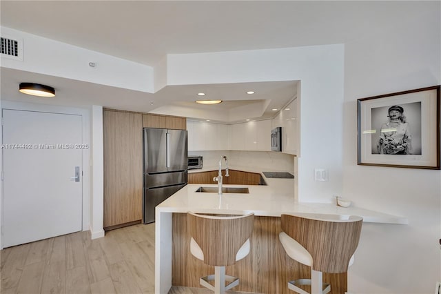 kitchen with appliances with stainless steel finishes, white cabinetry, sink, a kitchen bar, and kitchen peninsula