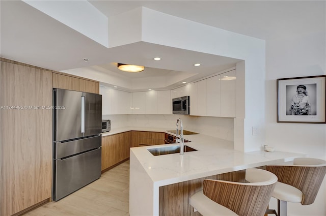 kitchen with a breakfast bar, white cabinetry, appliances with stainless steel finishes, kitchen peninsula, and light stone countertops