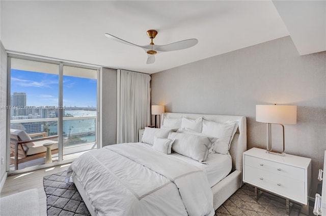 bedroom featuring dark hardwood / wood-style flooring, expansive windows, access to exterior, ceiling fan, and a water view