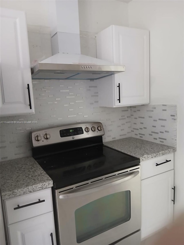 kitchen featuring stainless steel electric range oven, wall chimney exhaust hood, decorative backsplash, and white cabinets