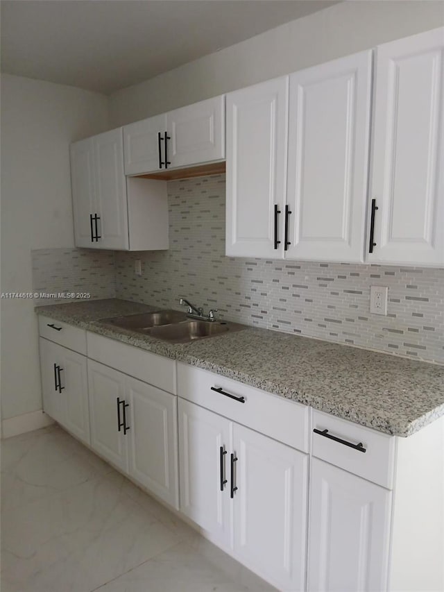 kitchen featuring a sink, white cabinets, marble finish floor, light stone countertops, and tasteful backsplash