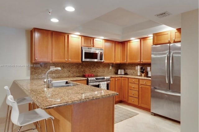 kitchen featuring sink, a breakfast bar, stainless steel appliances, light stone counters, and kitchen peninsula